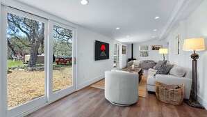 Un salón amplio con un ventanal grande, un sofá gris, un sillón blanco y una lámpara de pie.