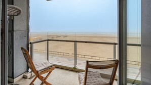 Ein Balkon mit zwei Holzstühlen und einem Tisch mit Blick auf einen Strand.