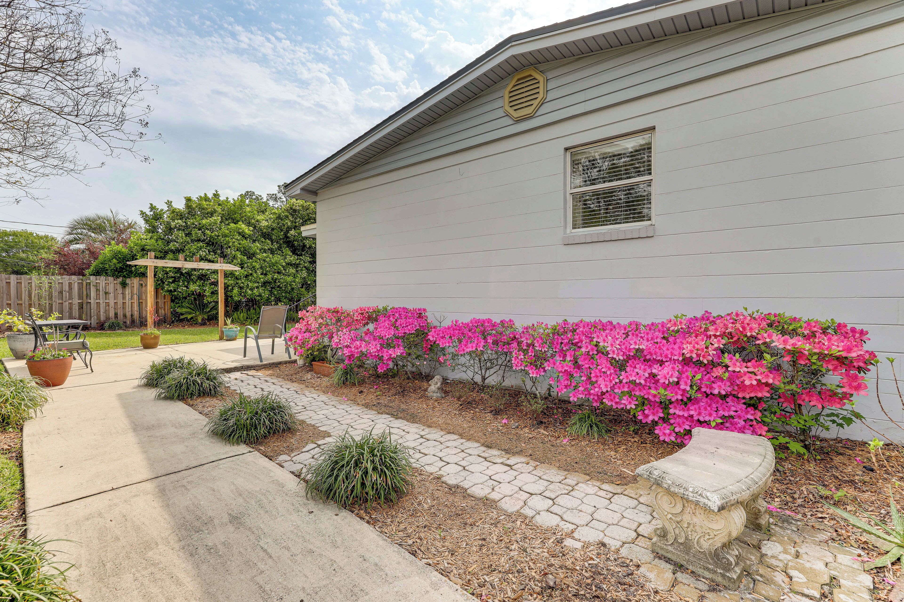 A residential house with a garden pathway, a pergola, and flowering bushes.