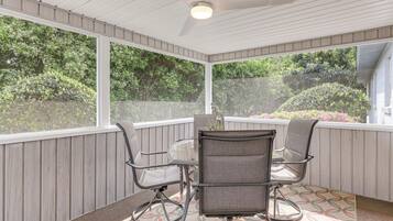 Relax in this serene outdoor space with a table for four and a ceiling fan overhead, surrounded by lush greenery.