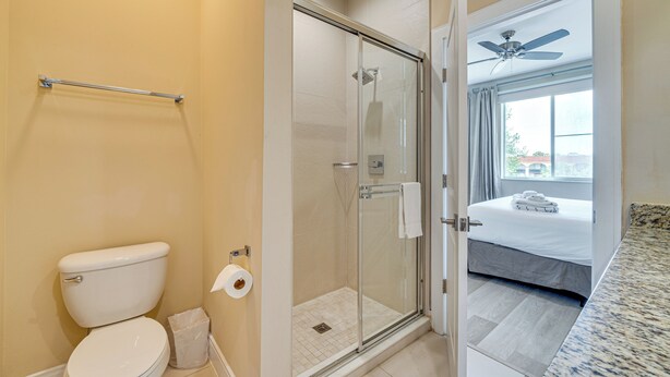 Une salle de bain avec des toilettes, une douche à parois de verre et un lit dans la pièce adjacente.