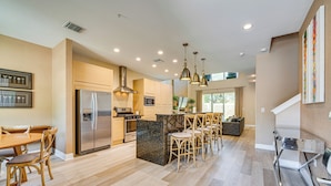 A modern kitchen with a central island, stainless steel appliances, and wooden chairs.