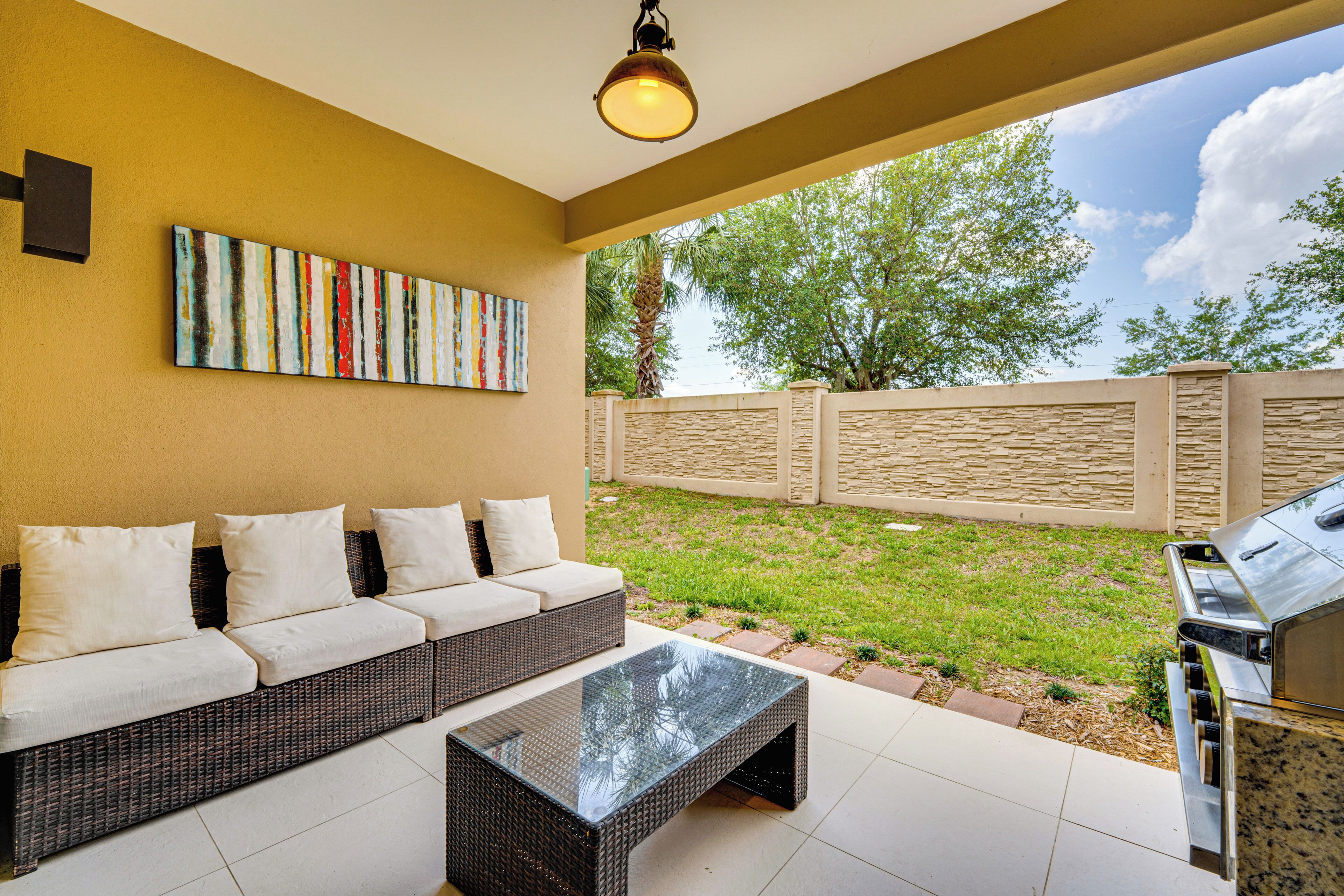 An outdoor patio with a wicker sofa, a glass coffee table, and a barbecue grill.