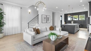 A modern living room with a grey sofa, a wooden coffee table, and a staircase leading to another level. - The Blackstone Manor (Atlanta)