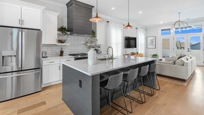 A modern kitchen with white cabinetry, stainless steel appliances, a large island with bar stools, and pendant lighting. - The Blackstone Manor (Atlanta)