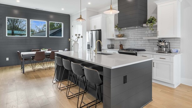 A modern kitchen with a large island, white cabinets, and a dark backsplash. - The Blackstone Manor (Atlanta)