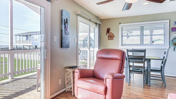 A room with a sliding glass door leading to a deck, a leather armchair, a dining table with chairs, and a ceiling fan. - Walk to Beach: Galveston Home w/ Patio & Balcony! (Galveston)