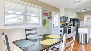 A kitchen with white cabinets, a black refrigerator, and a microwave. There are two windows with blinds, and a dining table with four placemats. - Walk to Beach: Galveston Home w/ Patio & Balcony! (Galveston)
