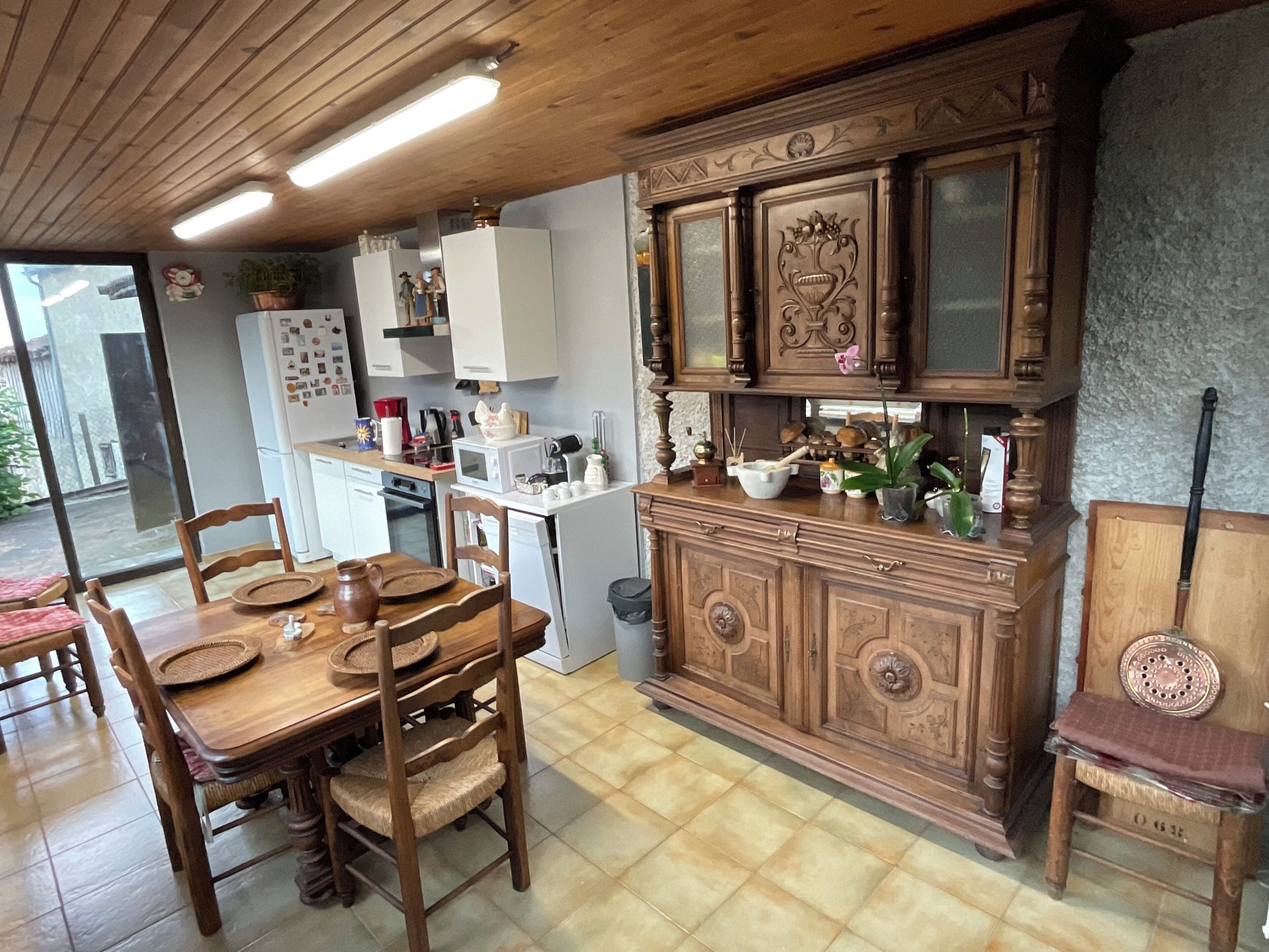 Een keuken met houten kastjes, een eettafel met stoelen en een uitzicht door een glazen deur.