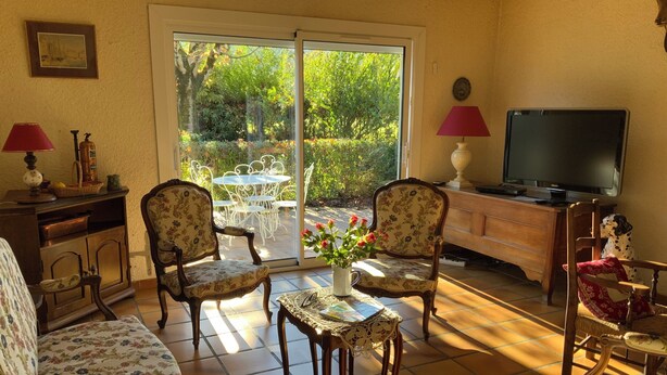 Un salon comprenant un canapé, deux fauteuils, une table basse, un téléviseur et une porte-fenêtre coulissante donnant sur une terrasse extérieure.