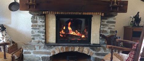 A stone fireplace with a fire, flanked by wooden chairs and a rustic decor.