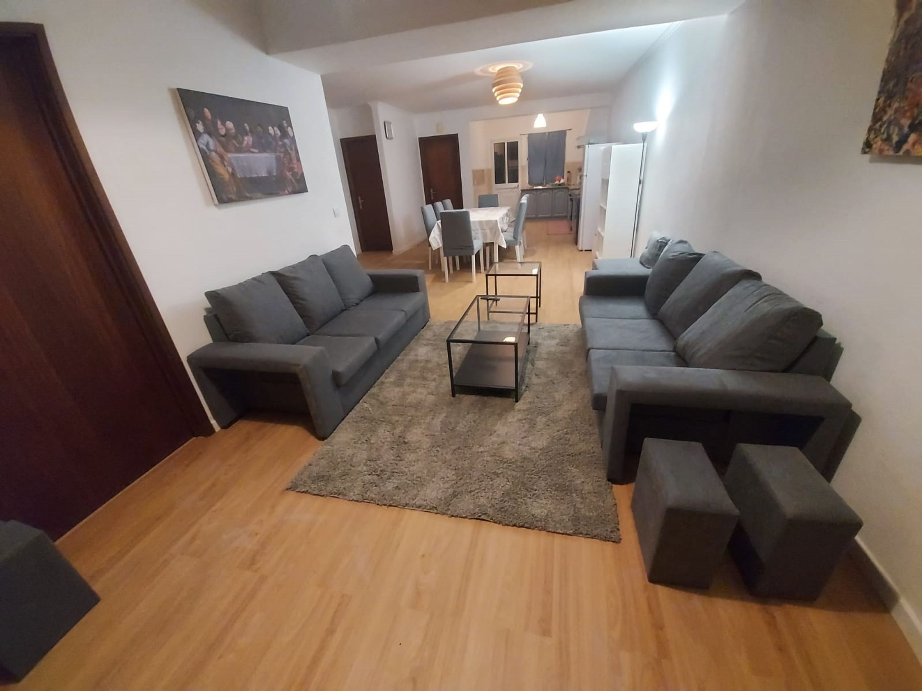 A modern living room with two sofas, a coffee table, and a rug. There is a dining area in the background with a table and chairs.
