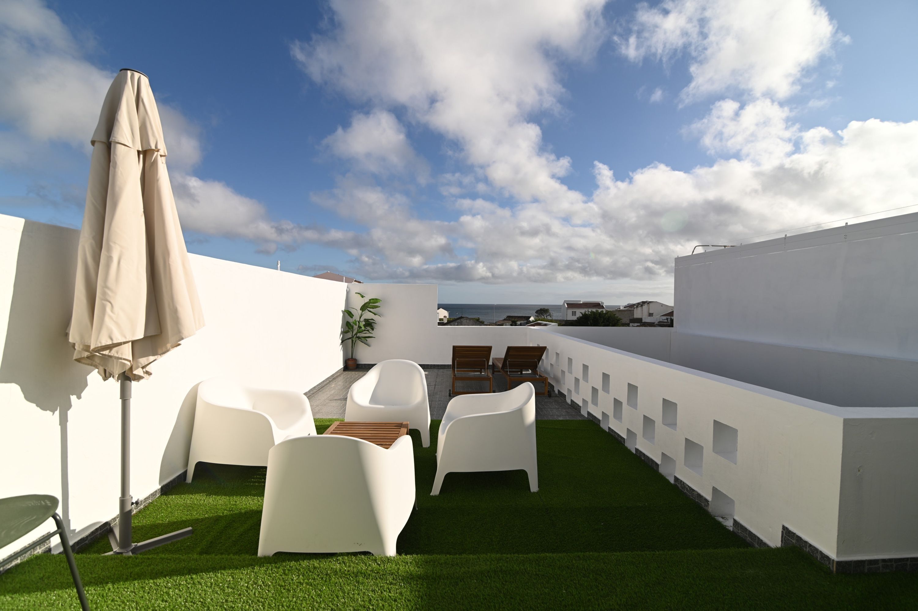 Una terrazza sul tetto con sedie bianche, un tavolo e un ombrellone color beige.