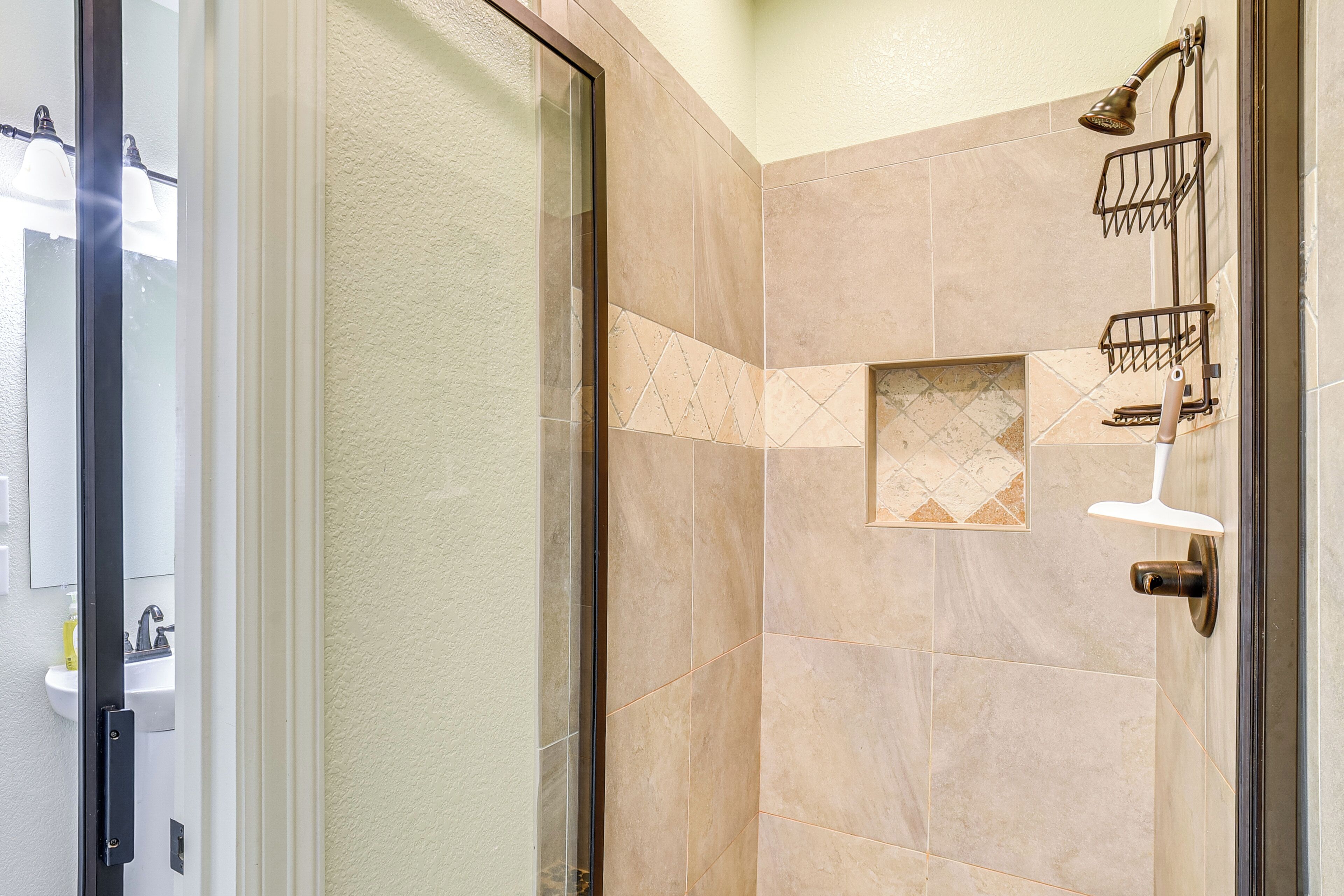 A shower area with a glass door, beige tiles, and a shower head mounted on the wall.