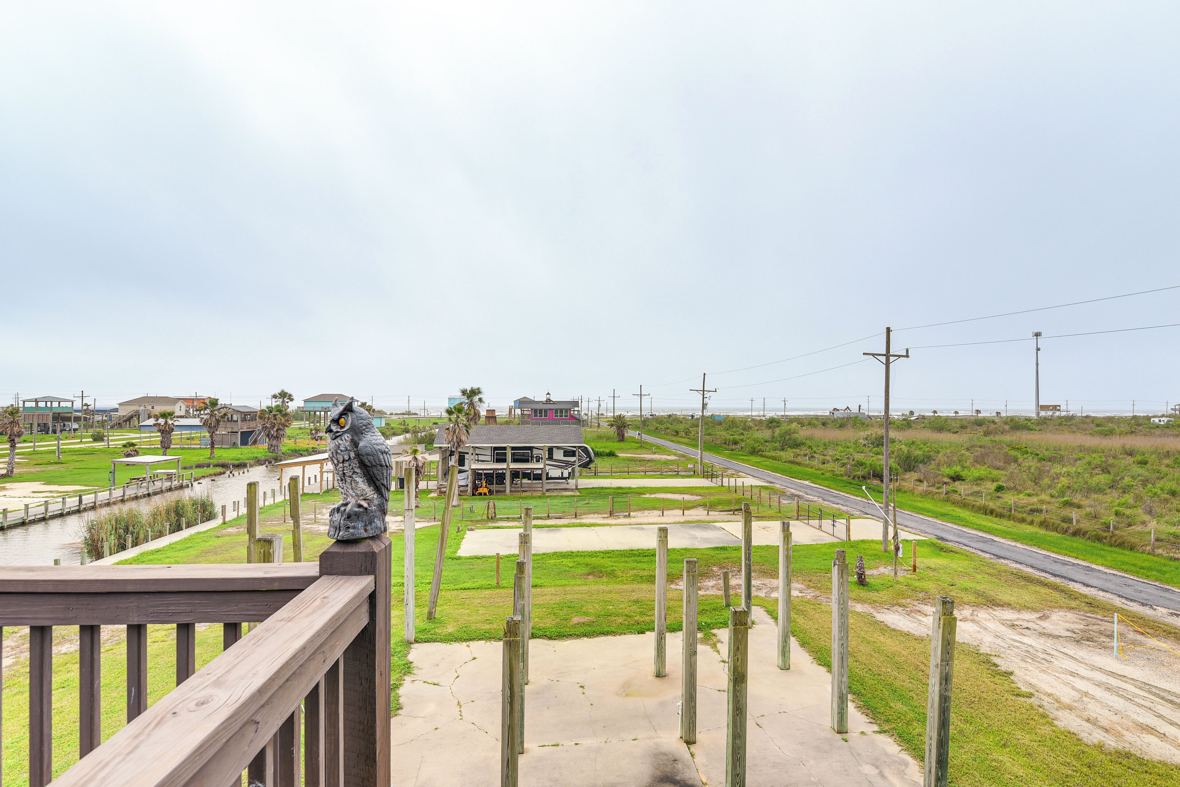 A view from a wooden deck overlooking a coastal area with a building, grassy fields, and a road.