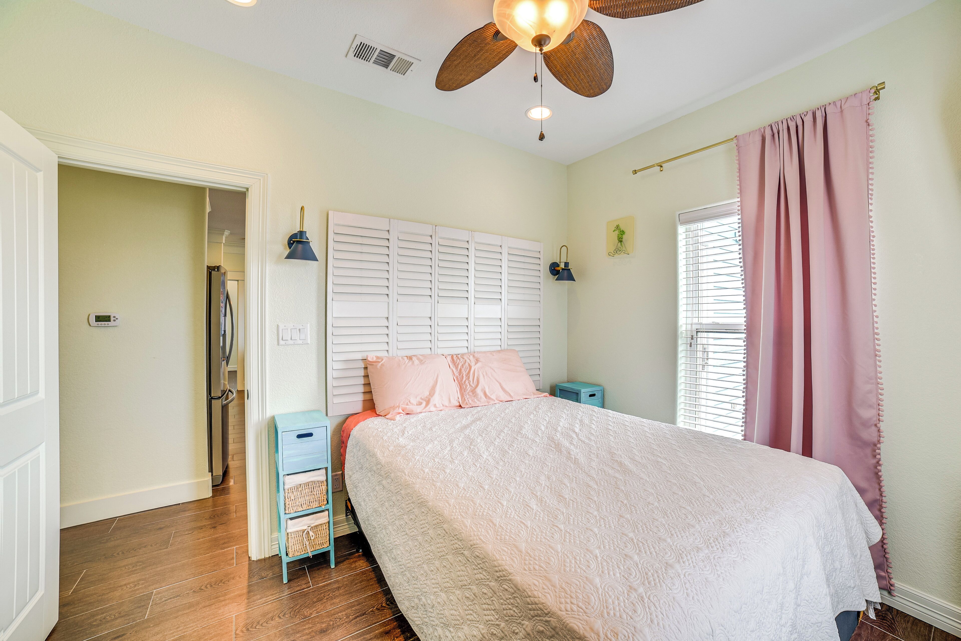 A bedroom with a bed, a ceiling fan, a window with curtains, and a door leading to another room.