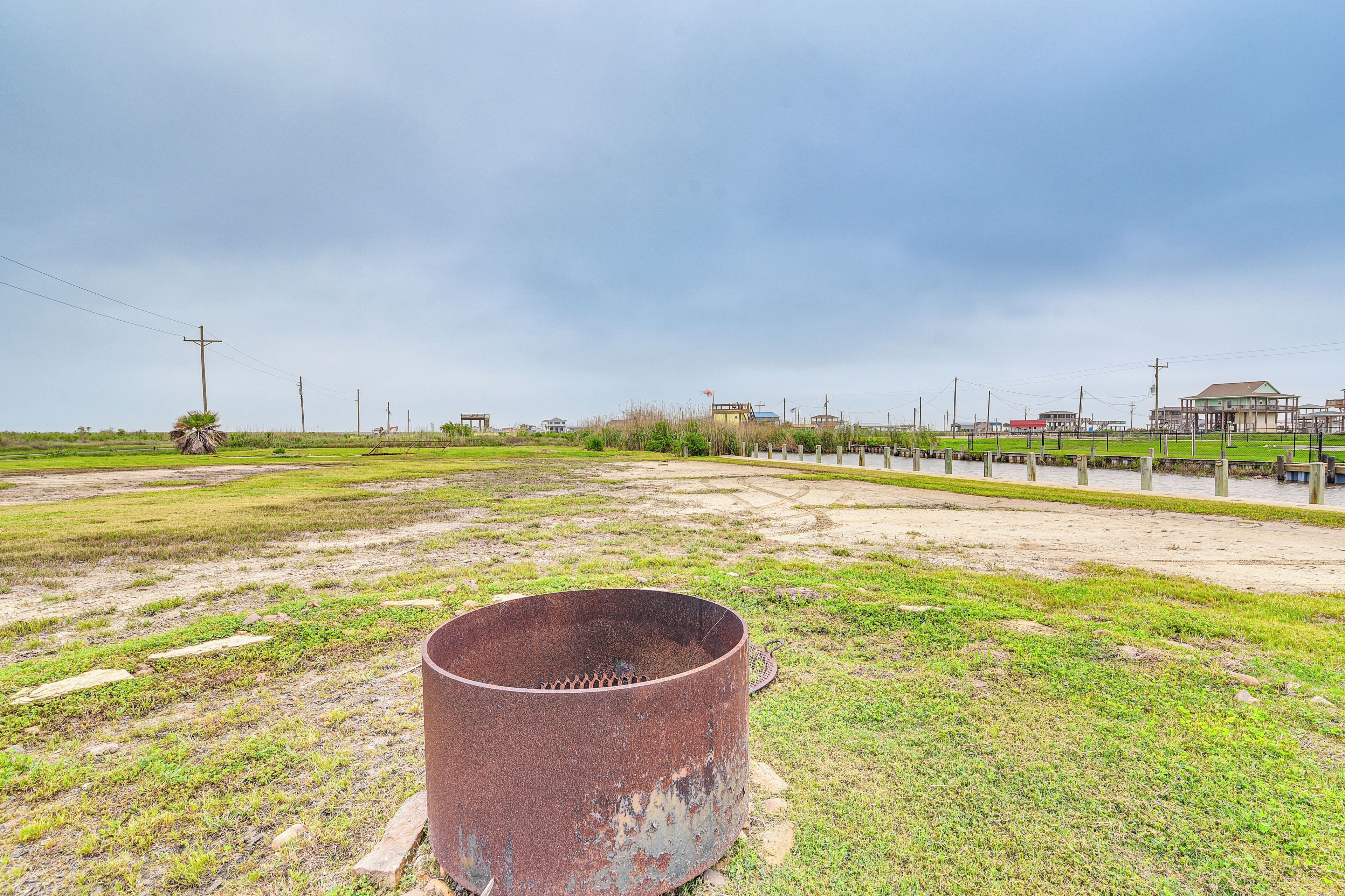 An open field with a large rusty metal structure in the foreground, a paved path, and a few buildings in the background.