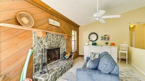 Ein gemütliches Wohnzimmer mit Kamin aus Stein, Holzwänden, einem blauen Sofa und einem Deckenventilator.