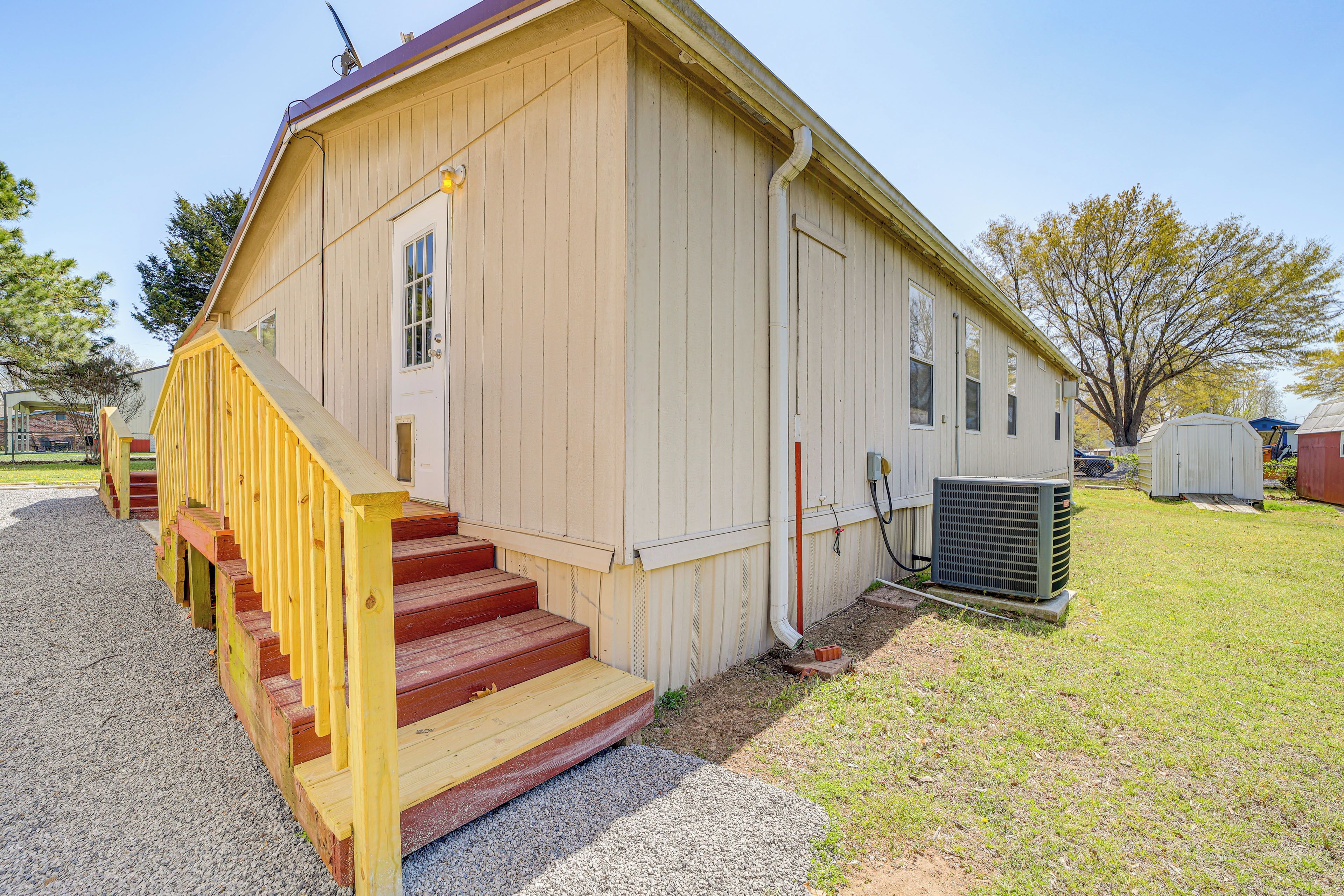 A single-story building with a wooden exterior, a set of red steps leading to a door, and an air conditioning unit on the ground.