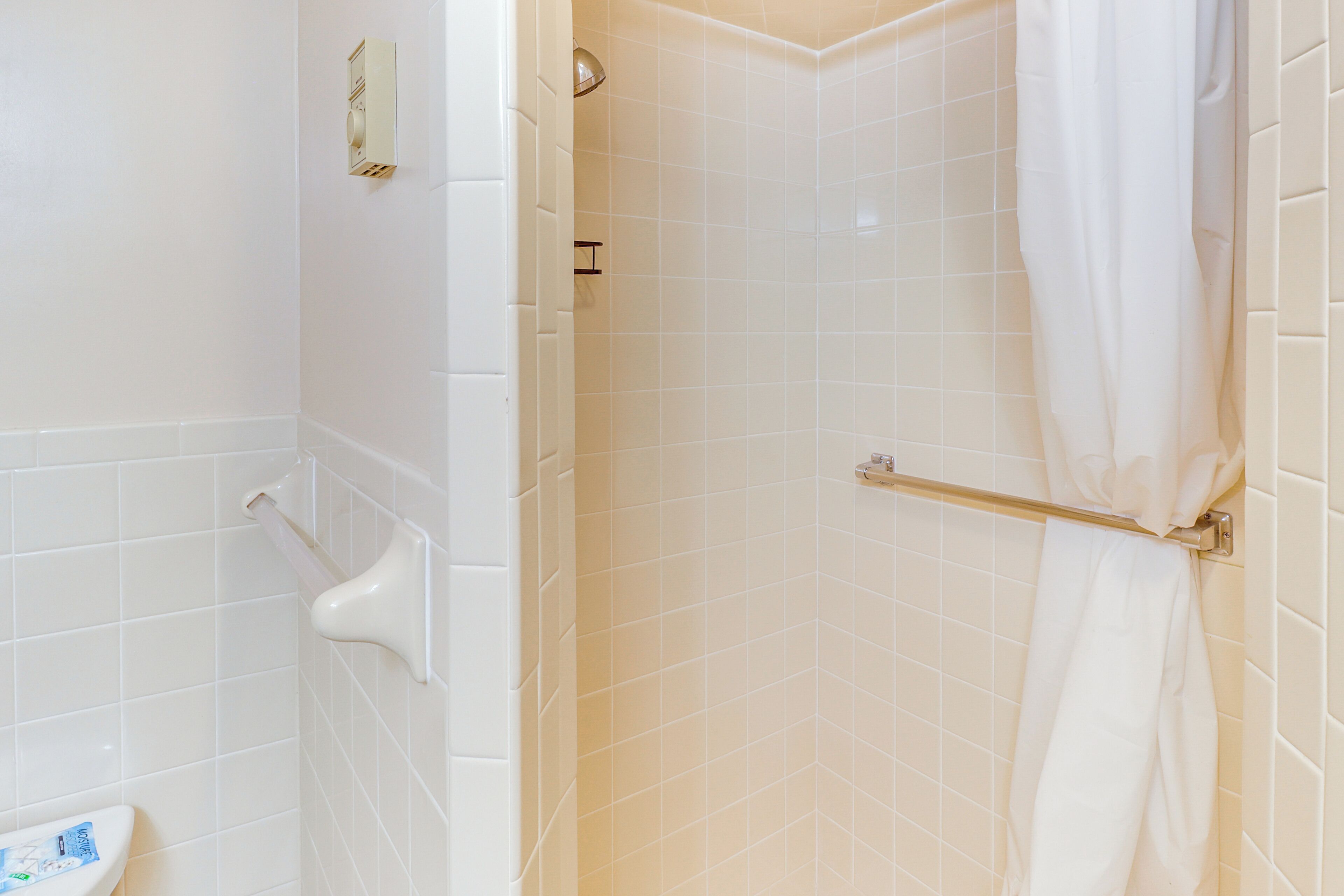 A bathroom with white tiles, a toilet, a shower with a towel rack, and a hand dryer.