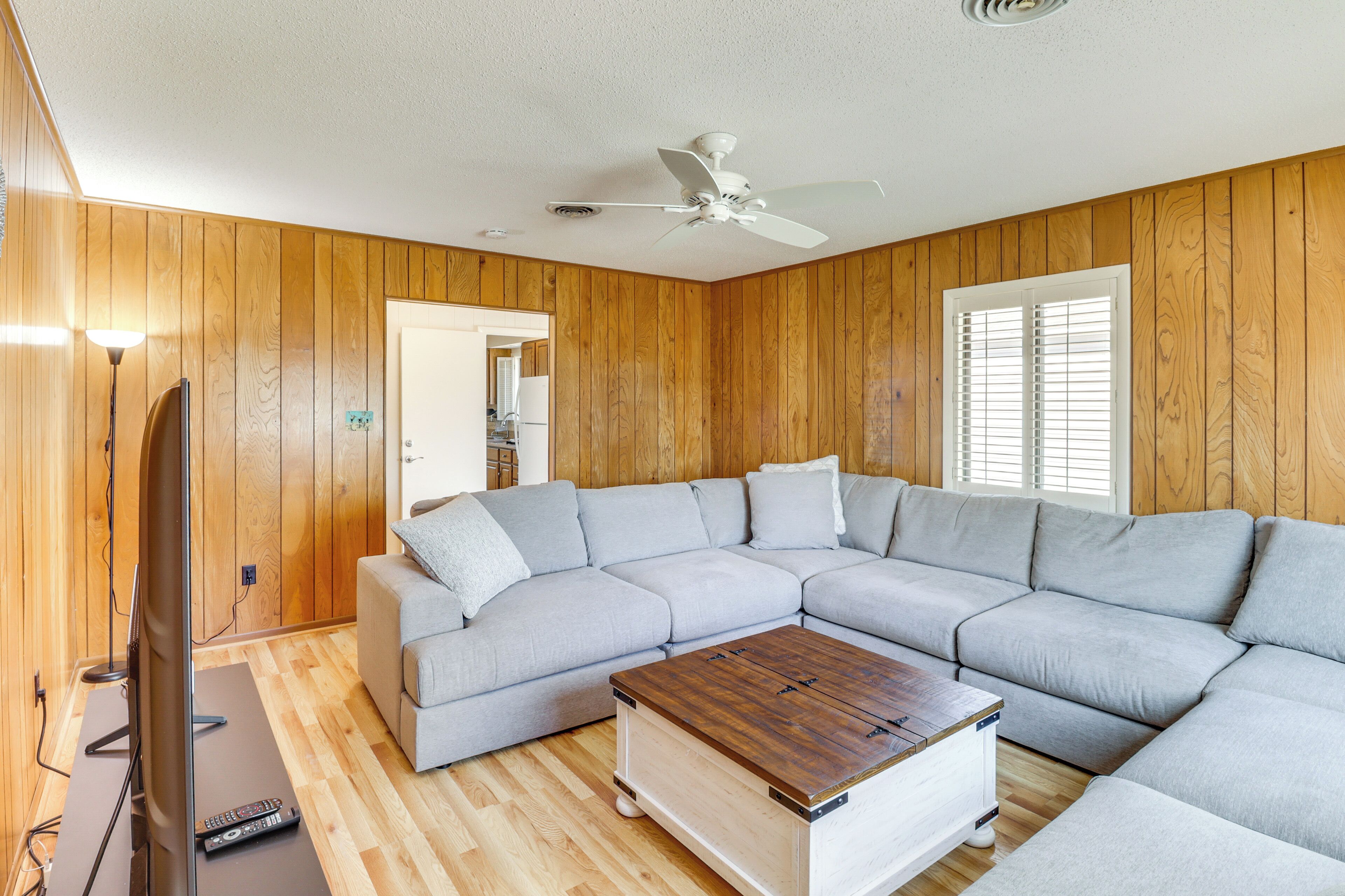 A living room with a sectional sofa, a coffee table, a television, and wooden walls.