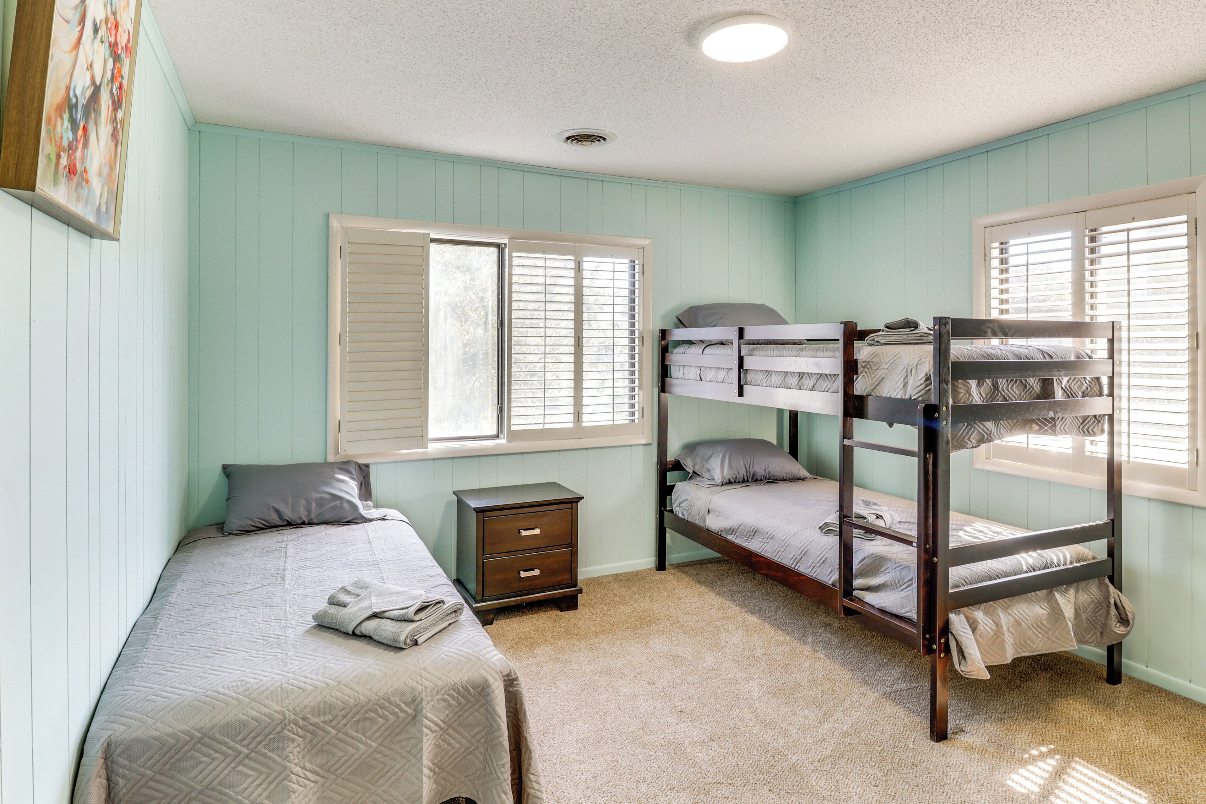 A room with bunk beds, a single bed, a nightstand, and a window with blinds.