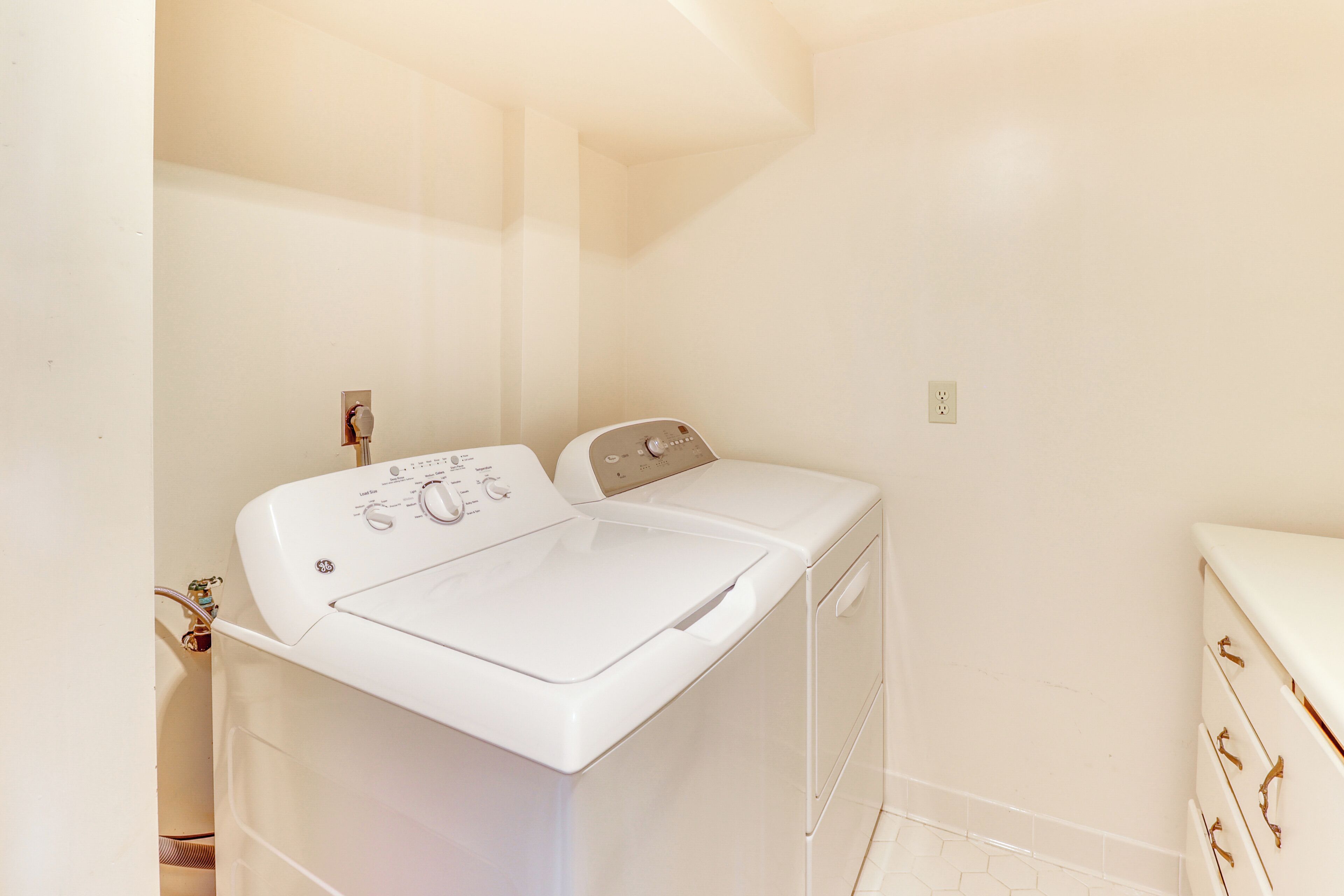 A laundry room with a front-loading washer and dryer, a small sink, and a countertop.