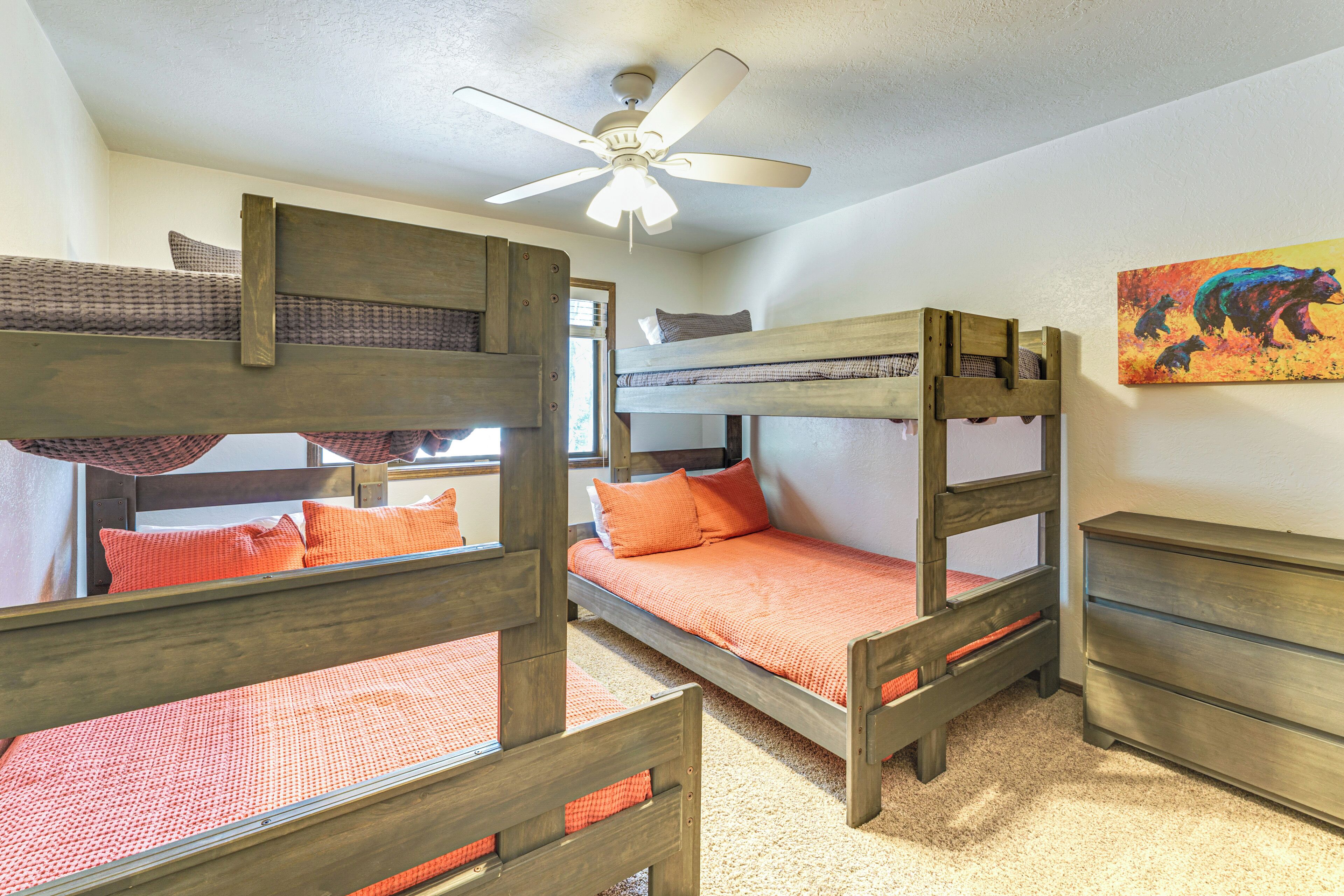 A room with bunk beds, a ceiling fan, a dresser, and a painting on the wall.