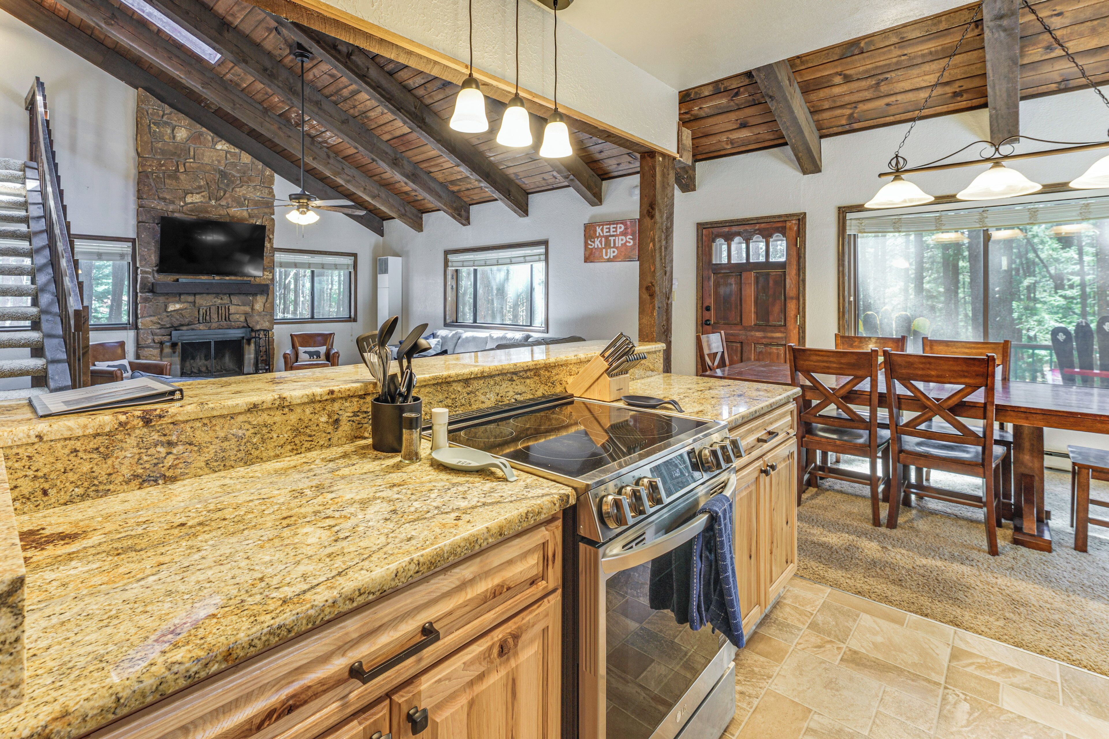 A kitchen with granite countertops, wooden cabinets, a stove, and a dining area with wooden chairs and a table.