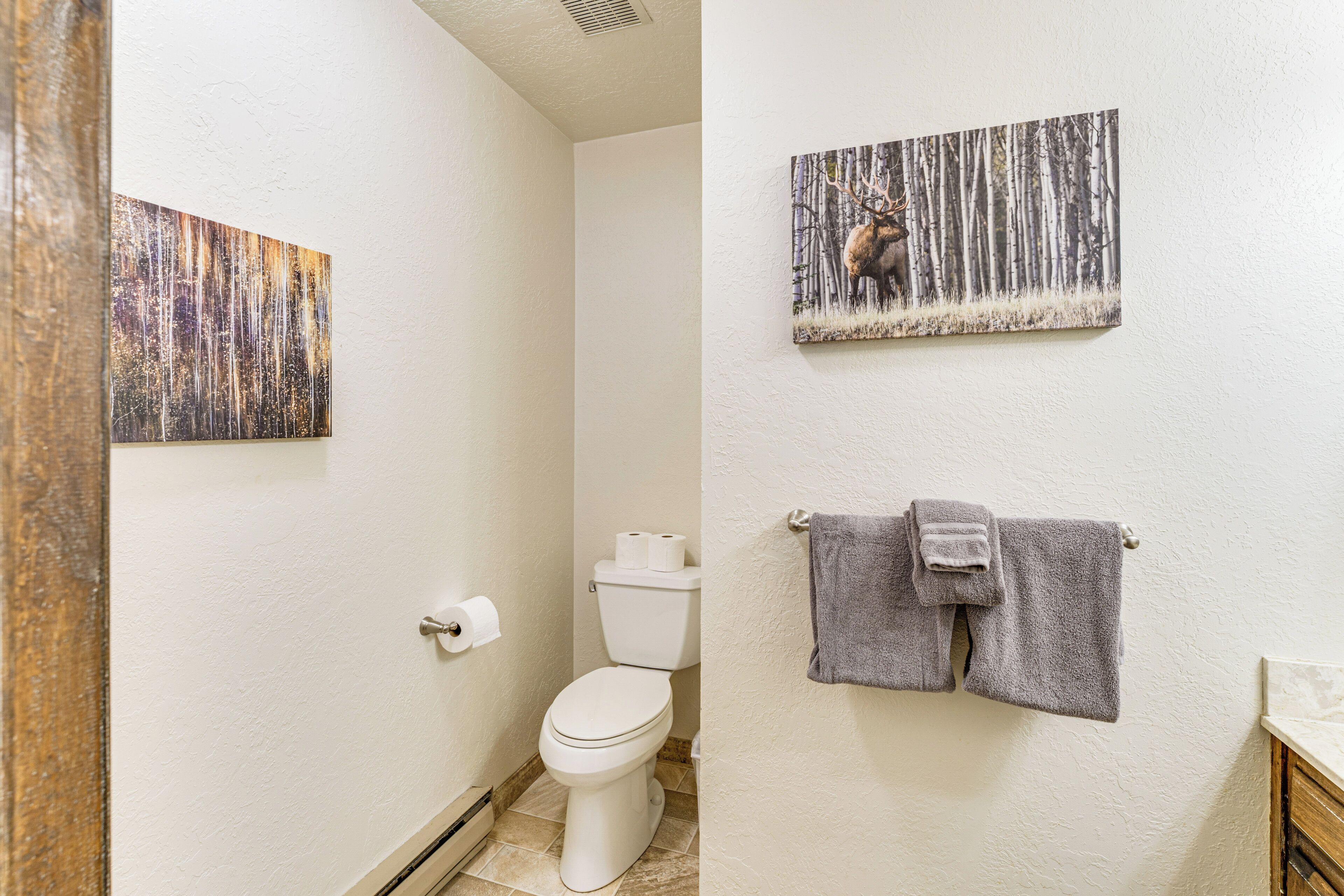 Une salle de bain comprenant des toilettes, un porte-serviettes avec des serviettes et deux œuvres d’art accrochées au mur.