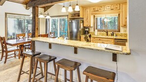 A kitchen with wooden bar stools, a large island, and a view of the forest through the window. - Walk to Lake & Trails: Angel Fire Home w/ Deck! (Angel Fire)