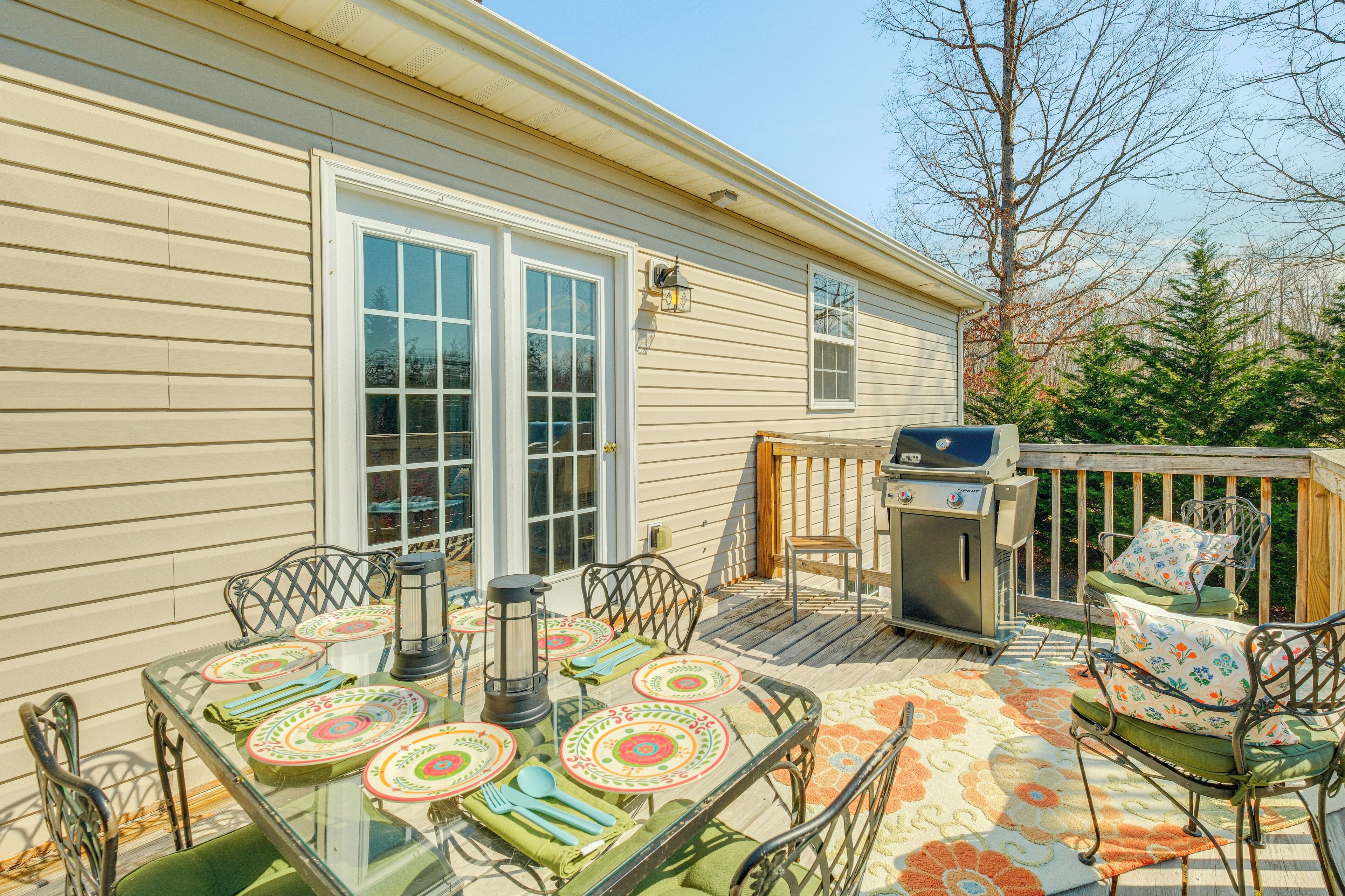 A deck with a glass table, metal chairs, and a grill.