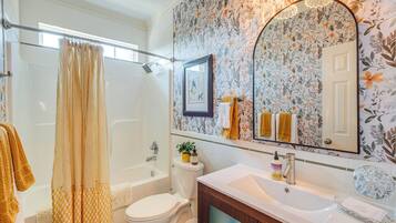 Baño con cortina de ducha, inodoro, bañera y lavabo con espejo encima.