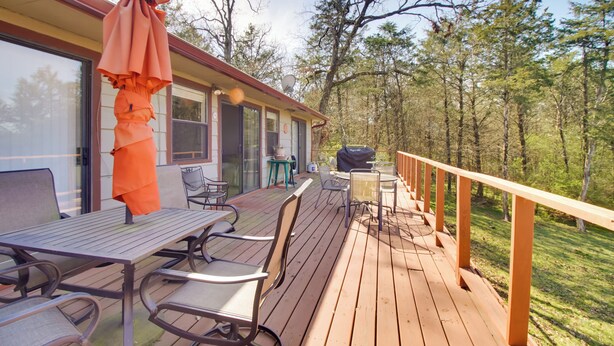 Une terrasse en bois, meublée pour l’extérieur, avec un barbecue et une vue sur la forêt environnante.