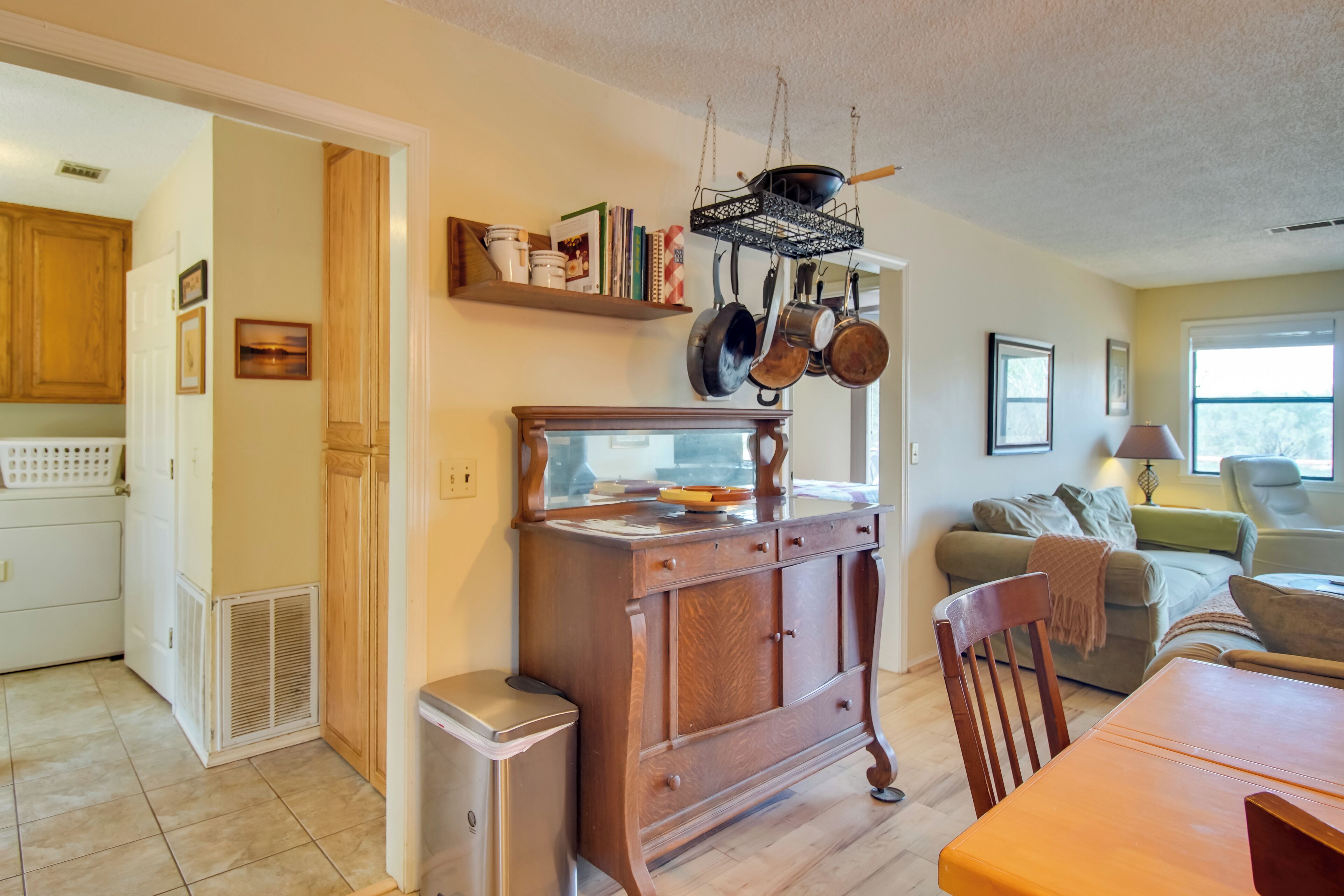 A kitchen with wooden cabinets, a dining table, and a living area with a sofa and a lamp.