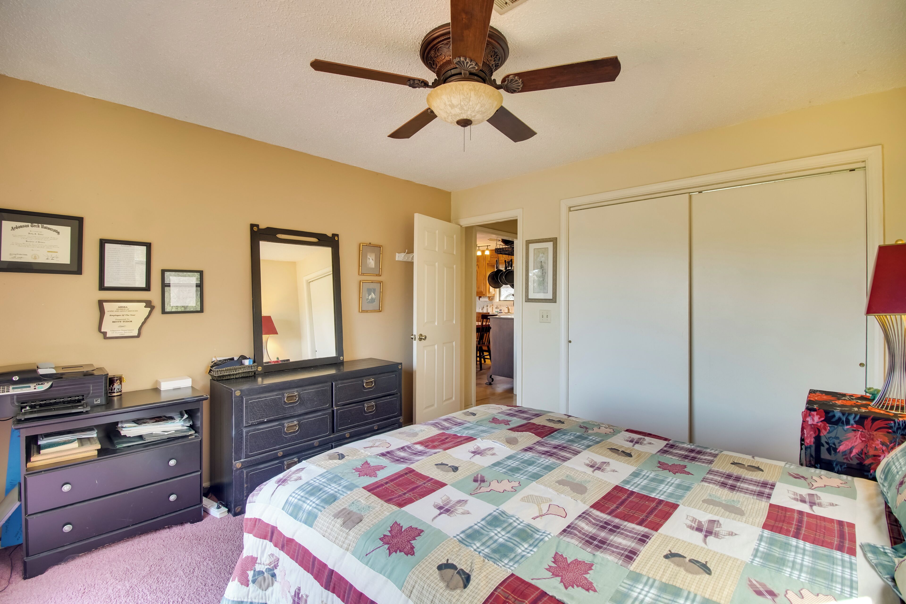 Une chambre à coucher comprenant un lit, une commode, un ventilateur de plafond et une porte donnant sur une autre pièce.
