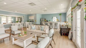 A spacious living area with a sofa, chairs, and a coffee table. There is a kitchen area with a refrigerator, stove, and bar stools.