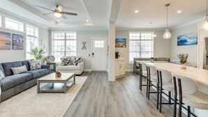 A spacious living room with a gray sofa, a coffee table, and a dining area with bar stools.