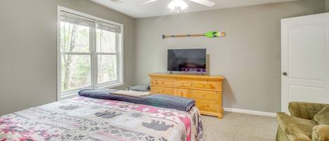 A bedroom with a bed, a ceiling fan, a TV on a wooden dresser, and a window with blinds.
