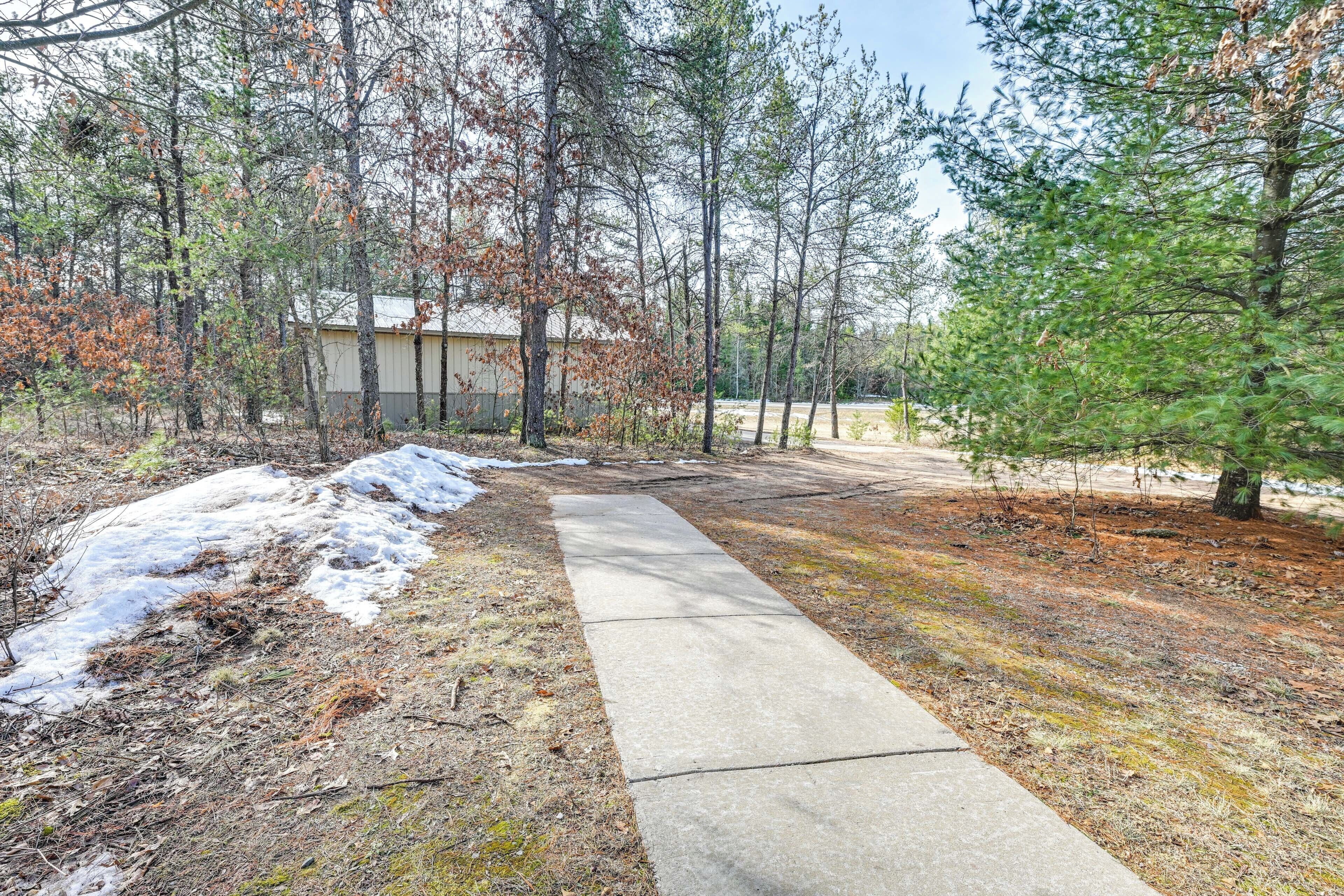 A concrete path leading to a building surrounded by trees, with some snow patches visible.