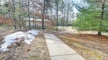 A concrete path leading to a building surrounded by trees, with some snow patches visible.