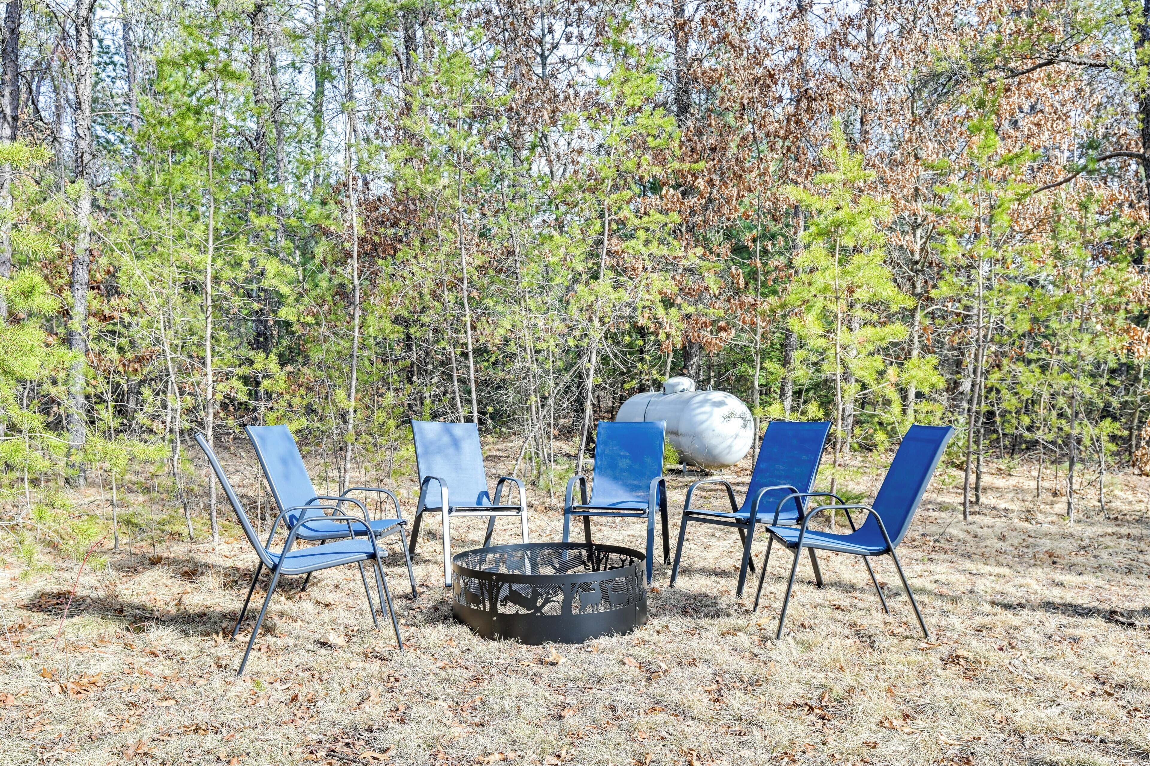 Un terrain de camping avec un foyer et quatre chaises bleues disposées autour.