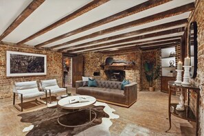A rustic living room with exposed brick walls, a leather sofa, a round coffee table, and a fireplace.