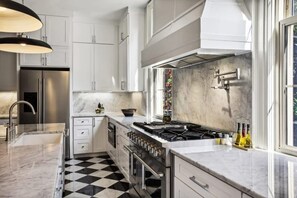 A modern kitchen with white cabinets, a black and white checkered floor, a stainless steel refrigerator, a gas stove, and a window with a view.