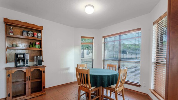 A dining area with a round table, chairs, a coffee maker, and a shelf with various items.