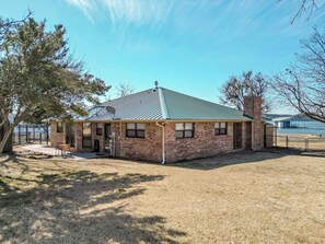 A single-story brick building with a metal roof, a satellite dish, and a fenced yard.