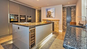 A modern kitchen with a central island, built-in ovens, and a stone accent wall. - Ttich Manor Retreat (Milton Keynes)