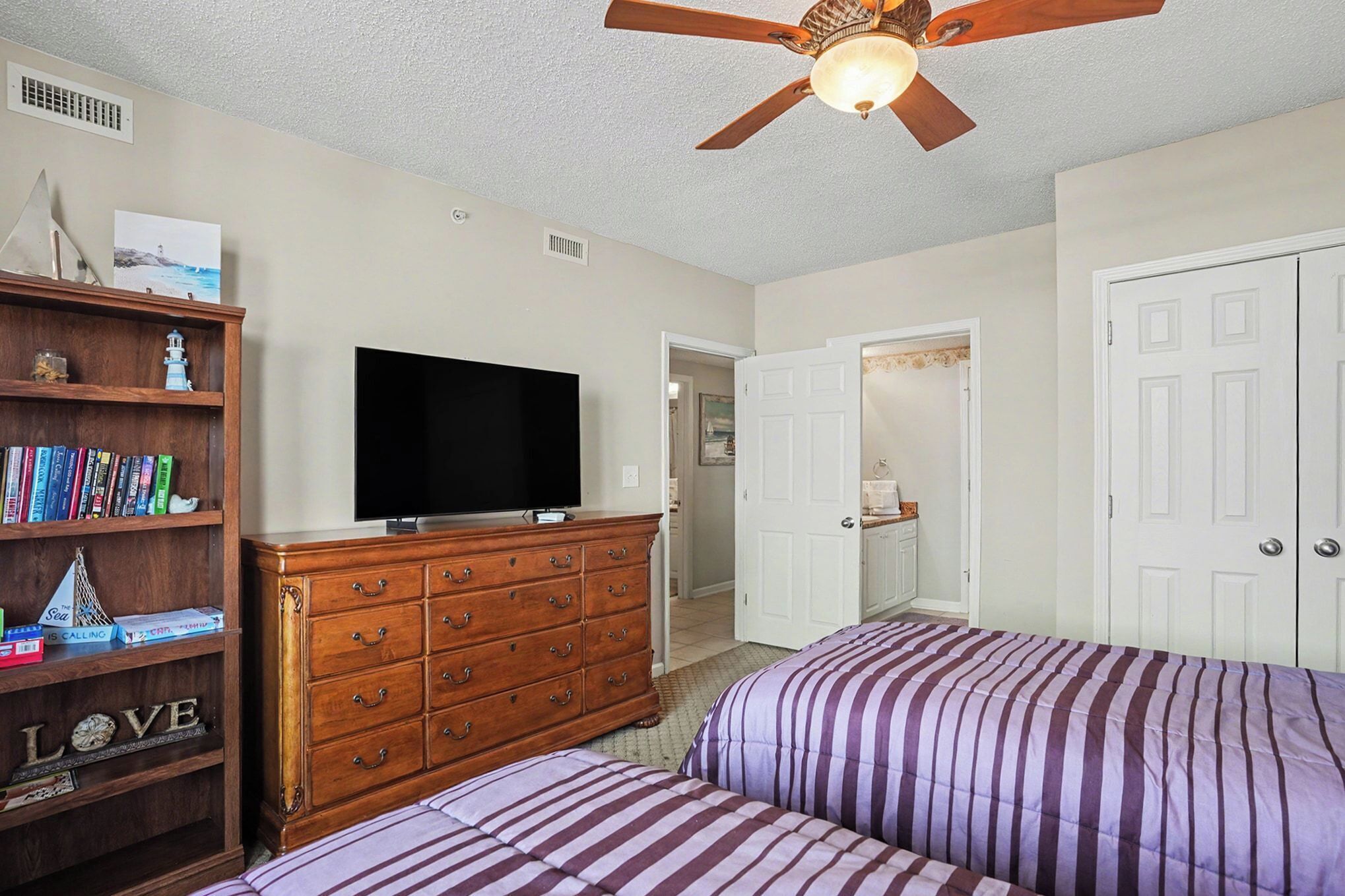 A bedroom with two beds, a TV, a wooden dresser, and a ceiling fan.