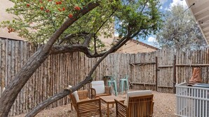 Una valla de madera, mobiliario de exterior y un árbol con flores rojas.