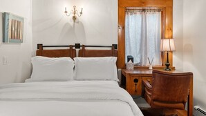 Un dormitorio con cama de madera, mesita de noche, silla, lámpara, luz de pared y ventana con cortinas.